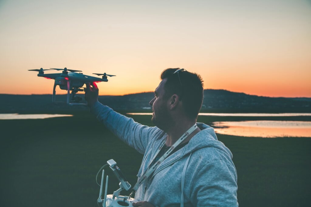 Drone pilot holding a quadcopter at arm’s length during sunset near the water in Lisbon.