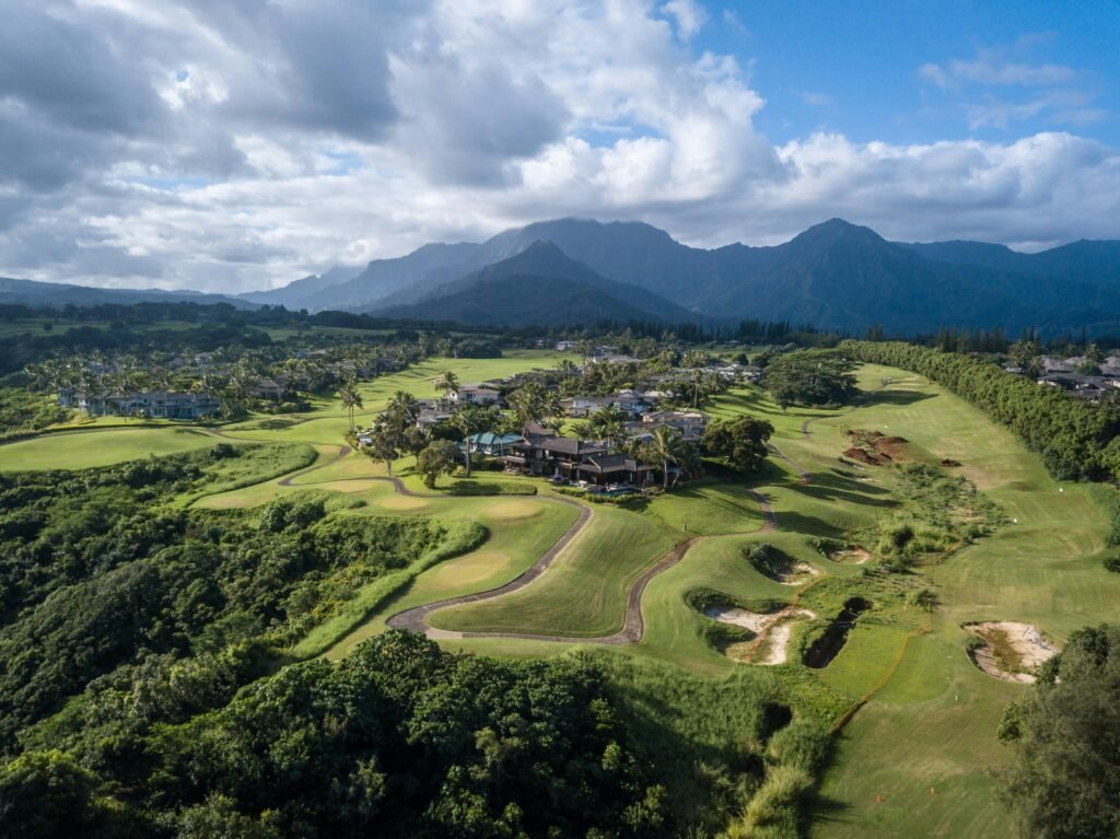 Drone shot of a green golf course and resort community with mountains in the background under a cloudy sky.