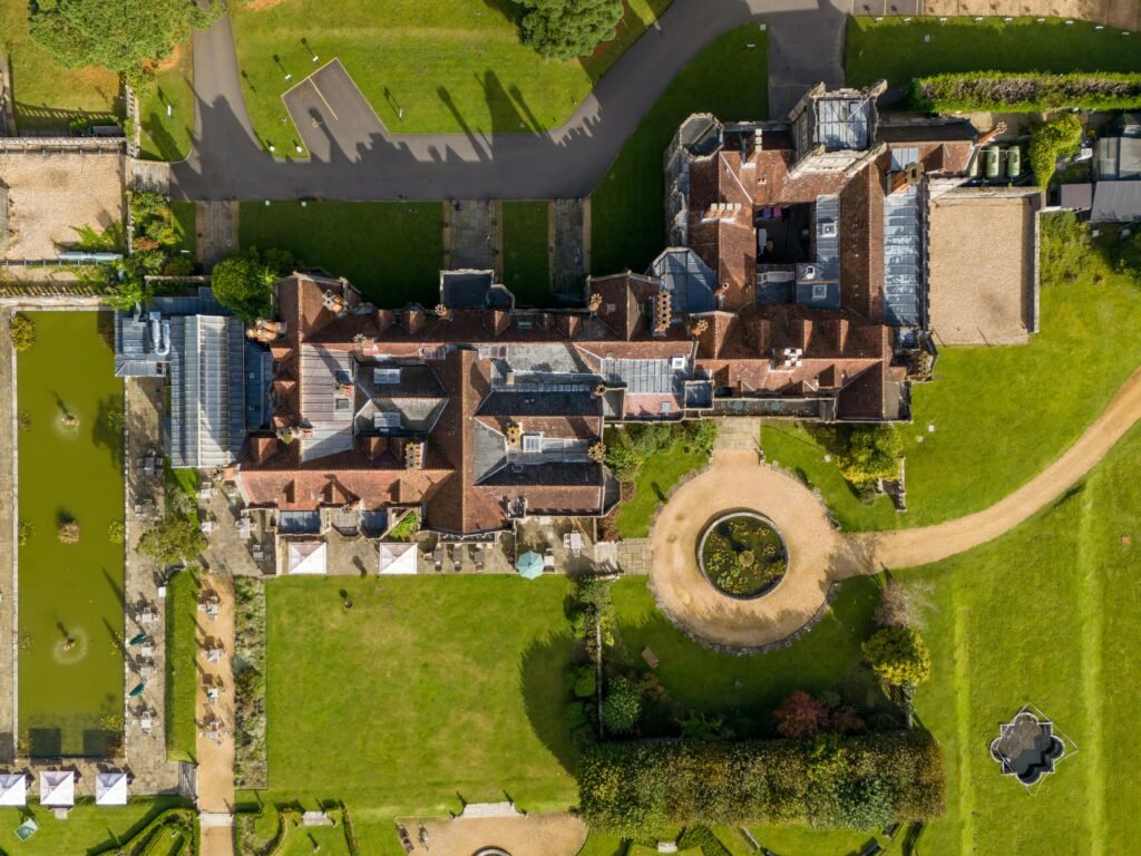 Aerial top‑down drone view of a large estate with historic main building, central circular driveway and landscaped gardens.